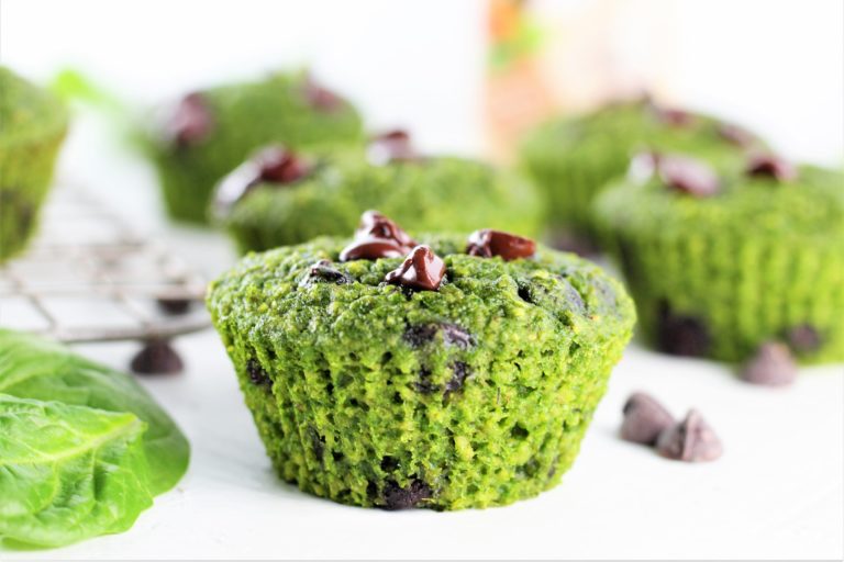 close up image of green oatmeal chocolate chip muffins with basil leaf and chocolate chips on counter
