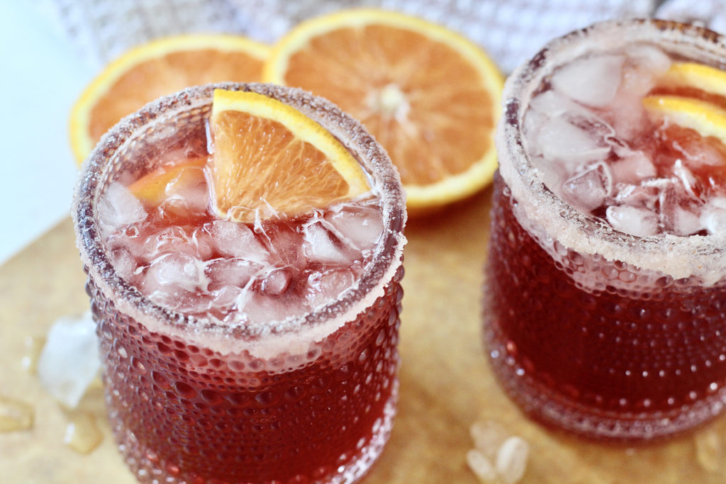 two pomegranate martinis with ice and orange wedges