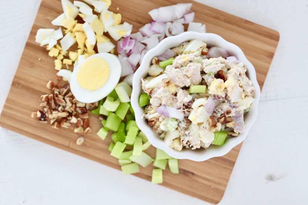 tuna salad in a white bowl on cutting board with hard boiled eggs celery, pecans, 