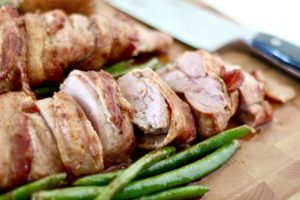 bacon wrapped grilled pork tenderloin with green beans on cutting board