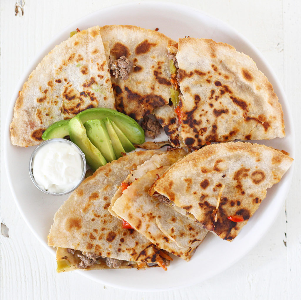 plate of beef quesadillas with avocado and sour cream