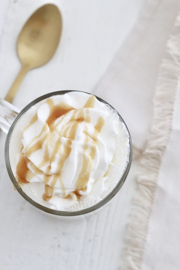 coffee drink with shipped cream and caramel sauce by a gold spoon