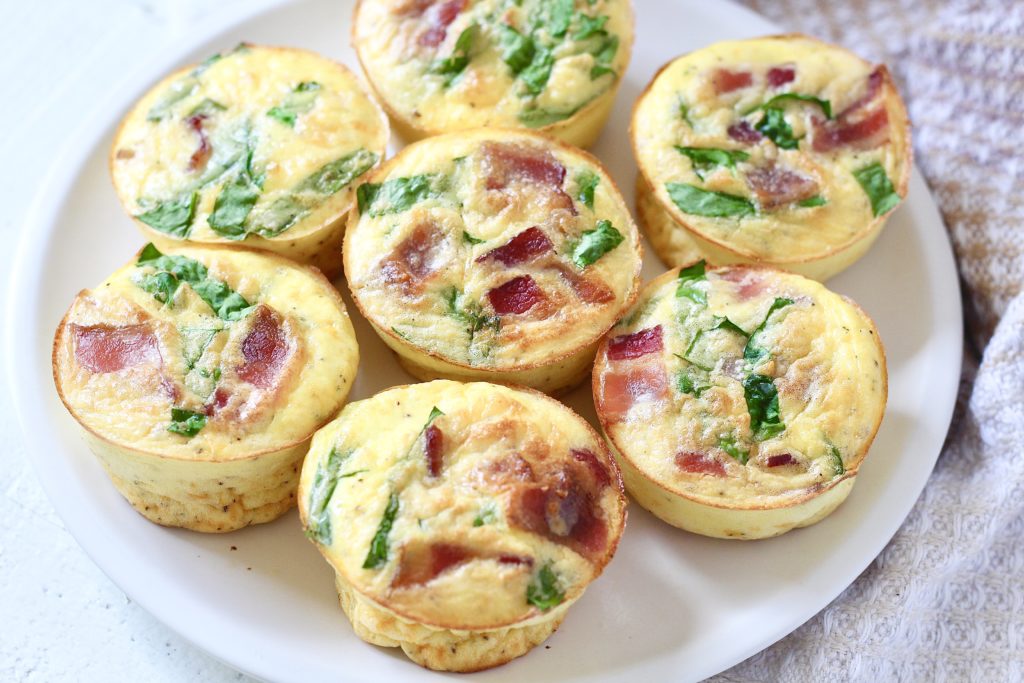 seven baked egg bites with spinach and bacon on white plate