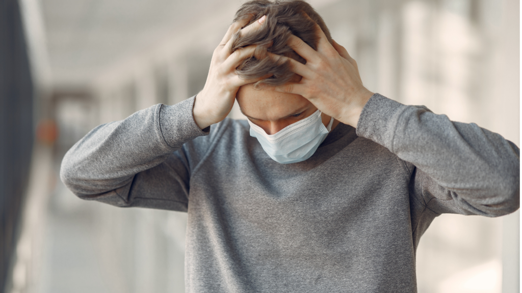 man wearing mask stressed out with hands on temple