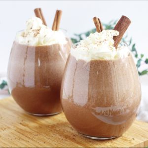 two glasses chocolate eggnog with whipped cream and cinnamon sticks