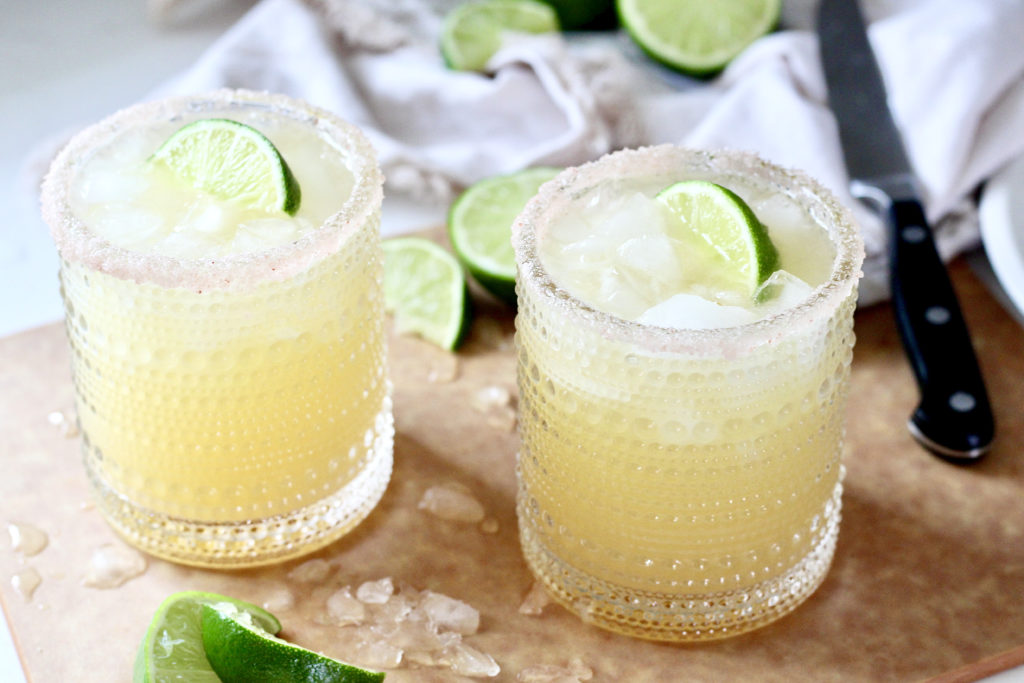 two skinny margaritas with lime wedges on cutting board