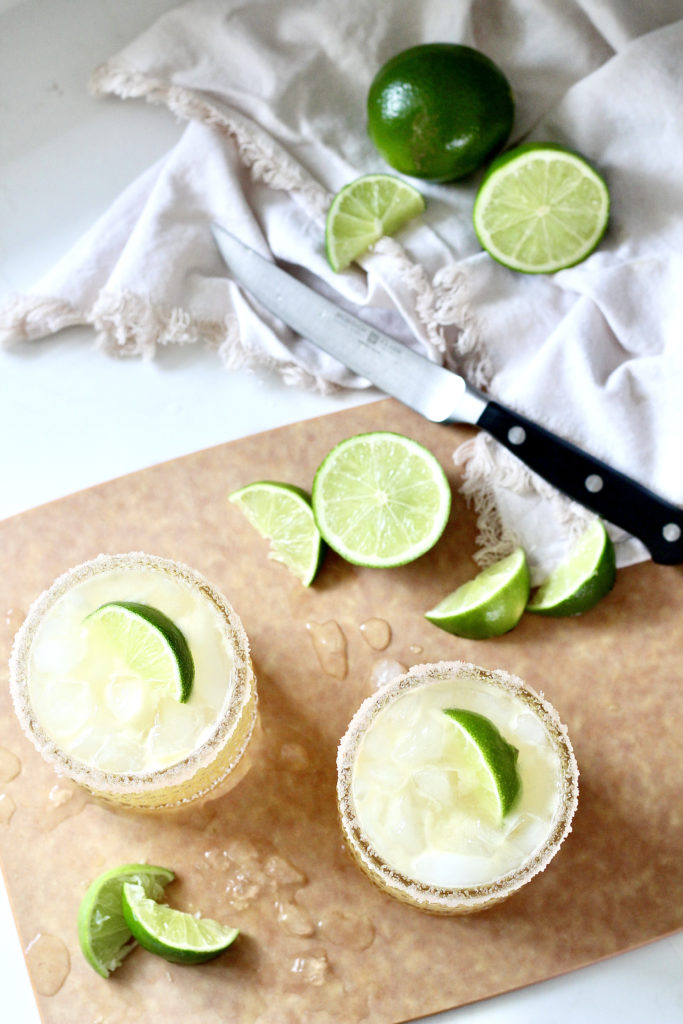 two margaritas on cutting board with limes