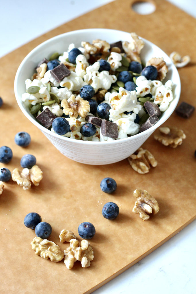 homemade trail mix in white bowl with blueberries walnuts and popcorn