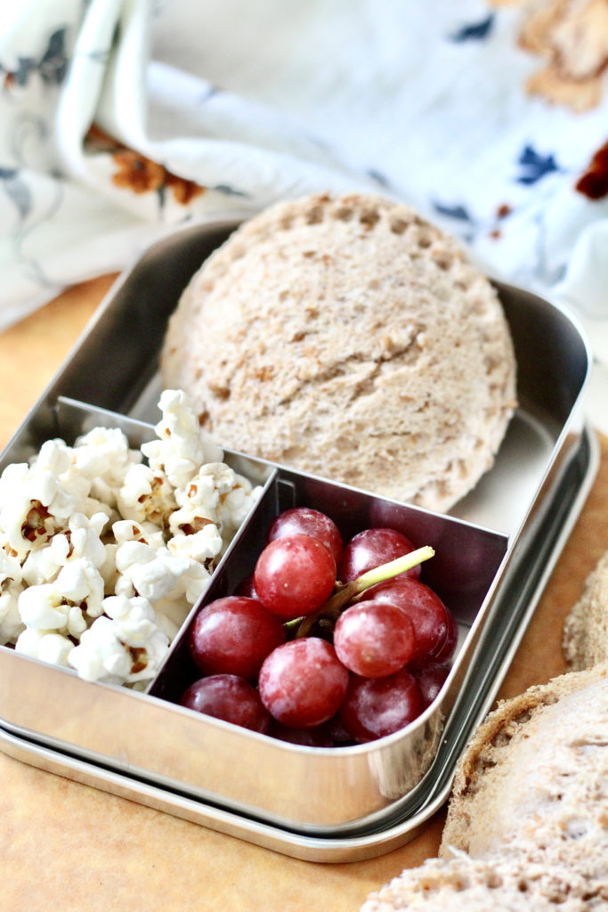 homemade uncrustable popcorn and red grapes in stainless steel bento box