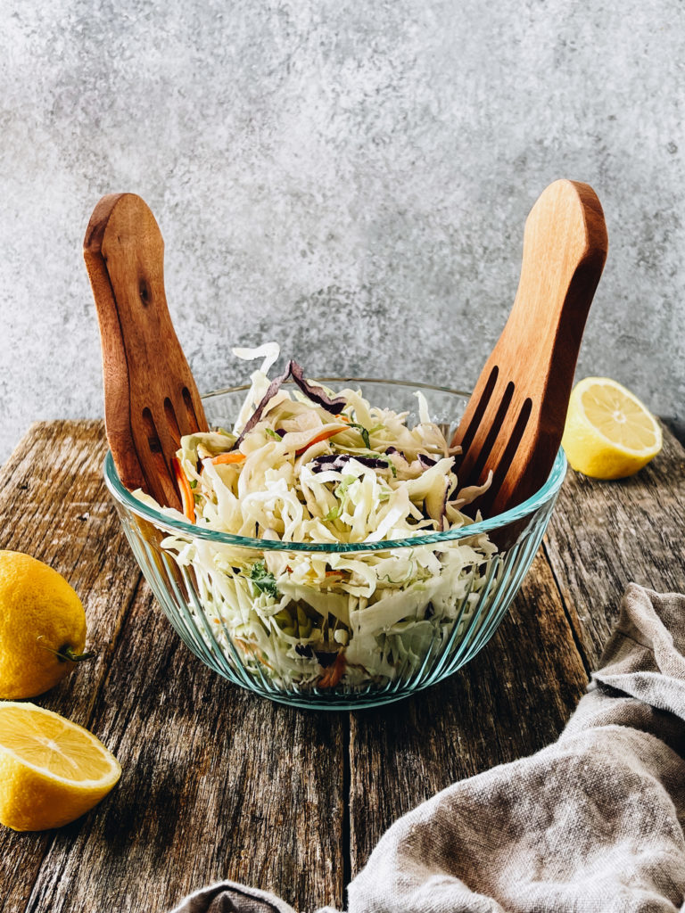 low carb coleslaw in glass bowl with wooden tongs