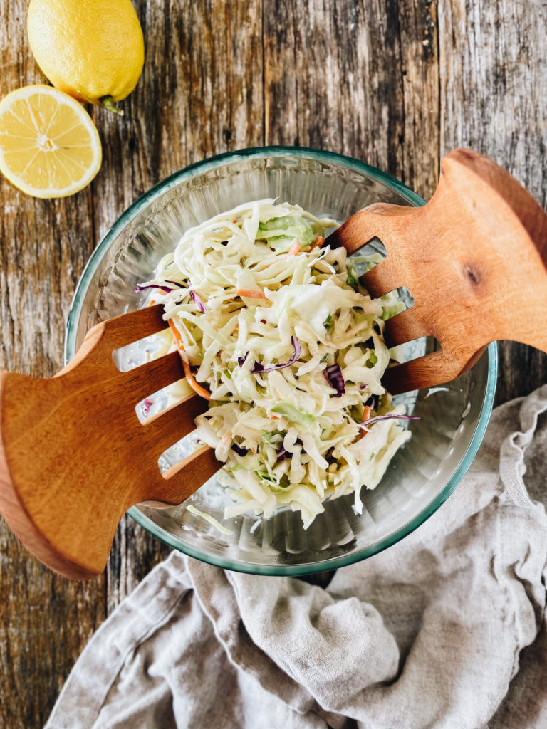 low carb coleslaw in glass bowl and wooden tongs