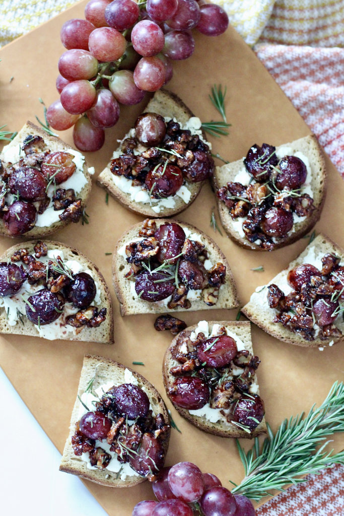goat cheese crostini with roasted grapes on cutting board with red seedless grapes