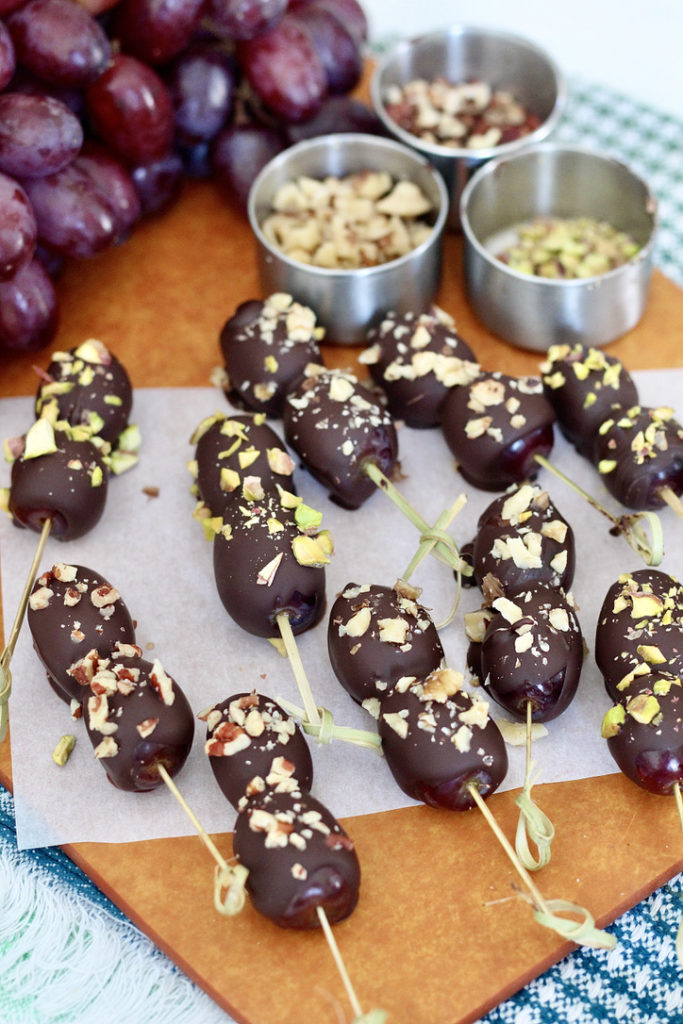dark chocolate covered grapes on cutting board with chopped nuts